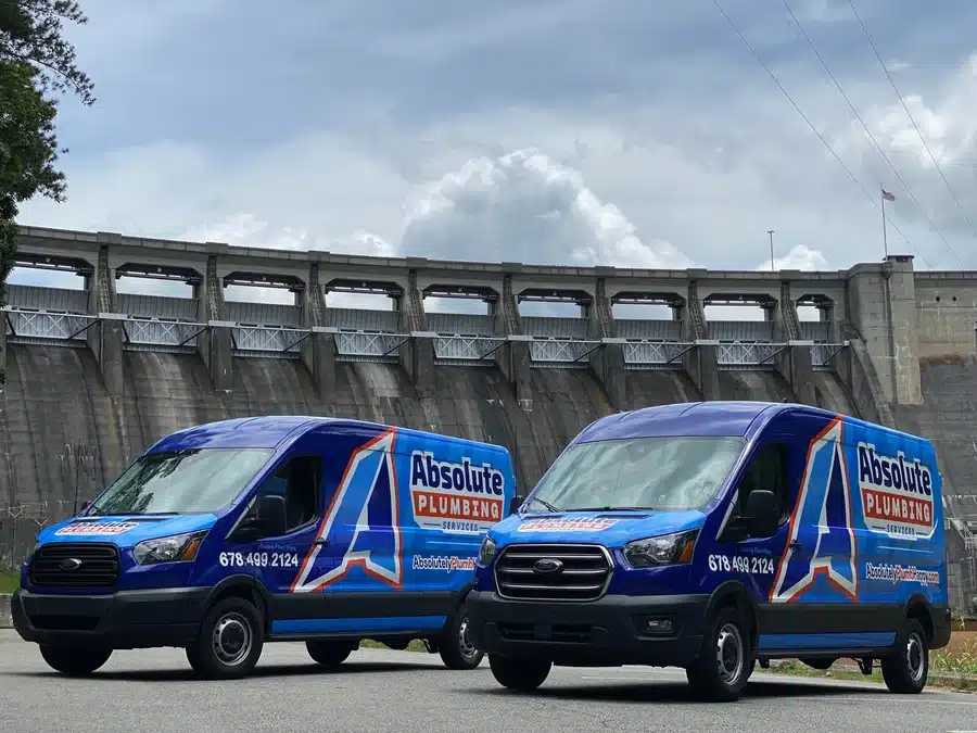 Two Absolute Pluming Vans parked outside near a dam in Acworth, GA